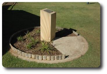 Sandstone block, 1 metre high, in circular garden with plaque on top
