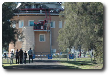 Side of circular building with people climbing stairs on outside to reach base of telescope mechanism