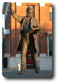 Full view of bronze statue, open book on left arm, right arm held up, hand open