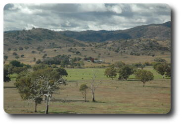 View over green or brown pasture, river not really visible, to farmstead and distant hills