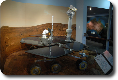Mars rover in display of simulated surface of Mars; side view