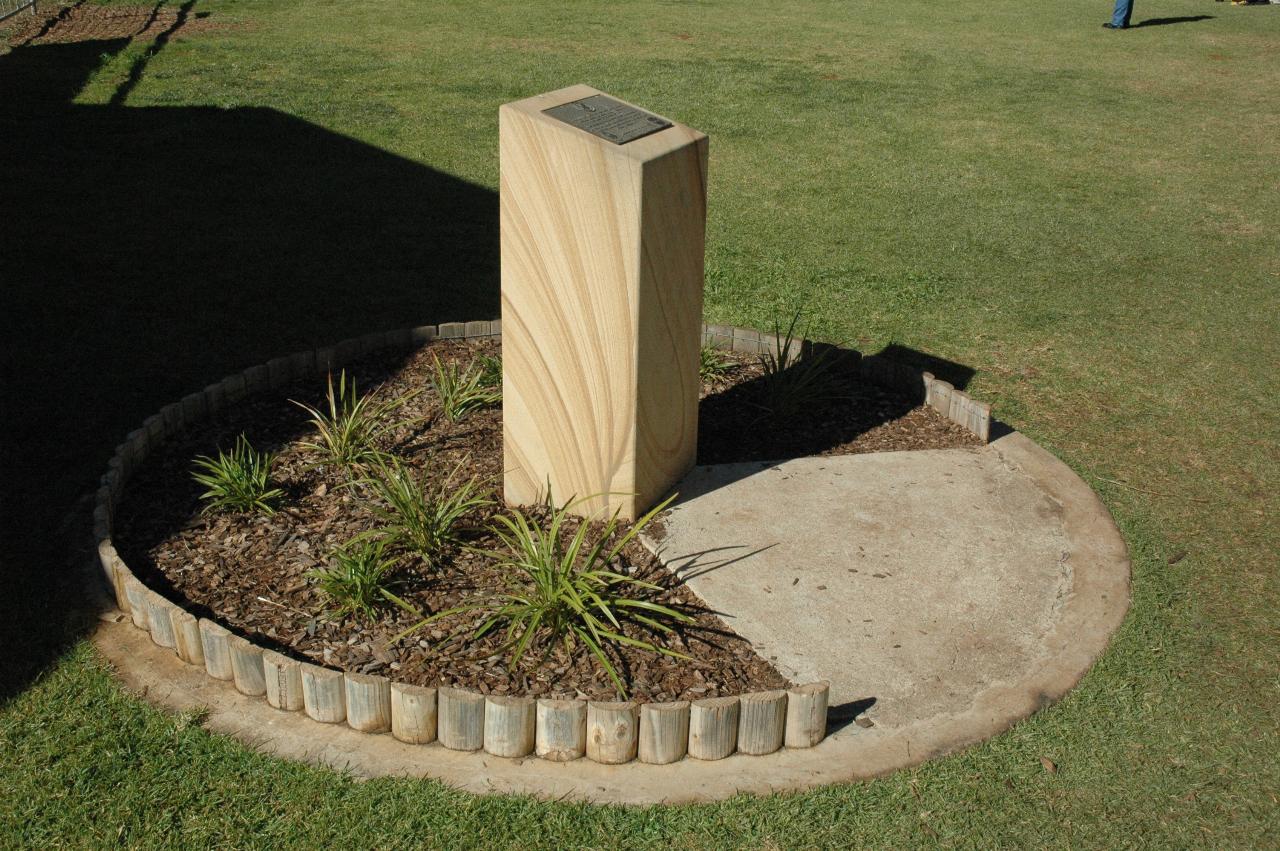 Sandstone block, 1 metre high, in circular garden with plaque on top