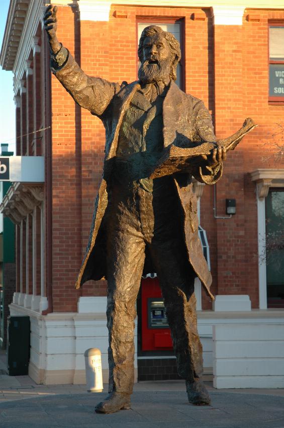 Full view of bronze statue, open book on left arm, right arm held up, hand open