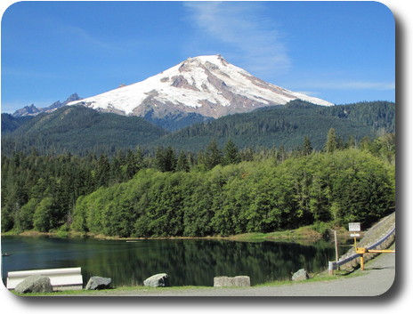 Snow capped mountain at end of summer with thick forest and pond in foreground