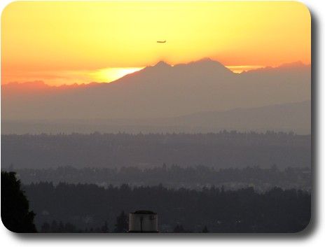 Sun setting behind distant mountains with plane flying past