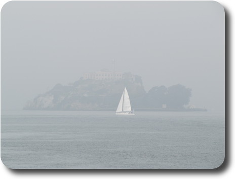 Sailing boat passing in front of fog shrouded island