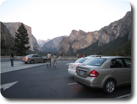 Car park with a few cars and people, and a valley without sun