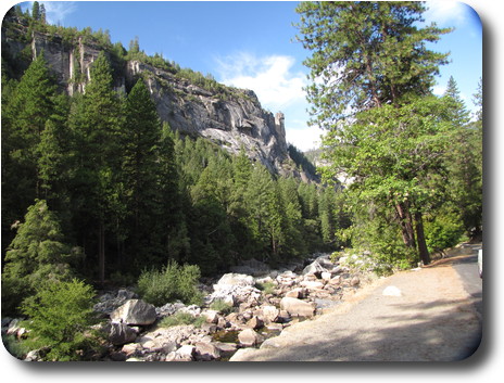 Along side a river with little water and rocky bottom, trees then sheer cliff
