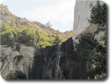 Very top of waterfall, with trees behind and a large rock formation behind them