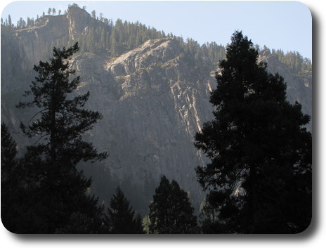 Steep, rugged cliffs behind darker trees still in shade