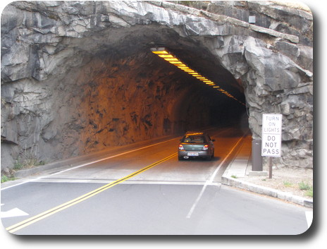 Car entering tunnel carved through the gray rock