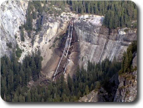 Distant waterfall down sloping rock face into tree lined base