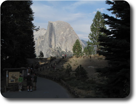 Gray domed rock beyond trees and people near visitor centre