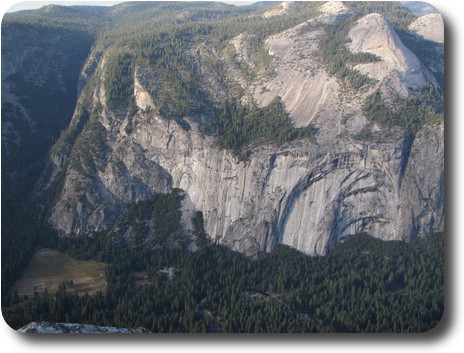 Tree covered valley floor with gray cliffs beyond and hills behind