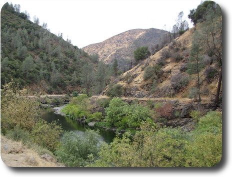 River in shallow valley with man made flat tracks on each side, and sparse hillside vegetation