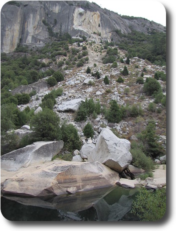 View over a pile of rocks and rubble to a gash on the cliff face from where it came