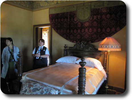 Bed against wall with semi-circular tapestry; tour guide and woman nearby