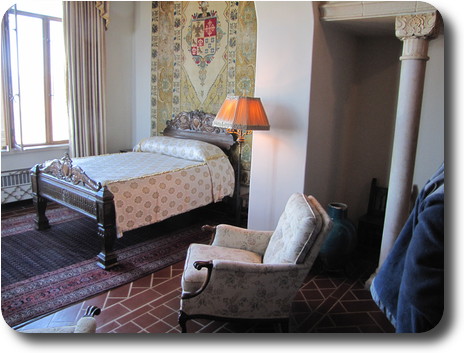 Double bed against tapestry hanging on wall; chair nearby and window on other side