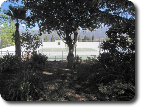 Garden in shade with double tennis court behind and distant hills