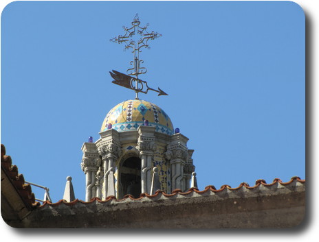 Tower with tiled dome on top, with a cross and wind direction indicator atop