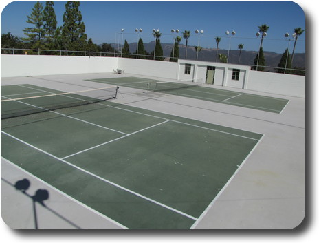 Twin tennis courts surrounded by lights with distant hills
