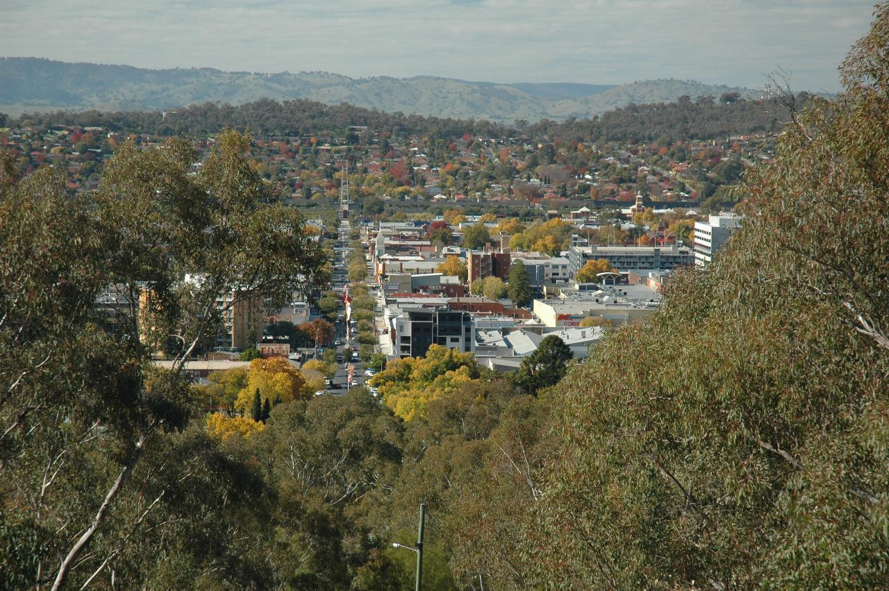 Distant street running away from camera towards distant hill with many buildings among trees