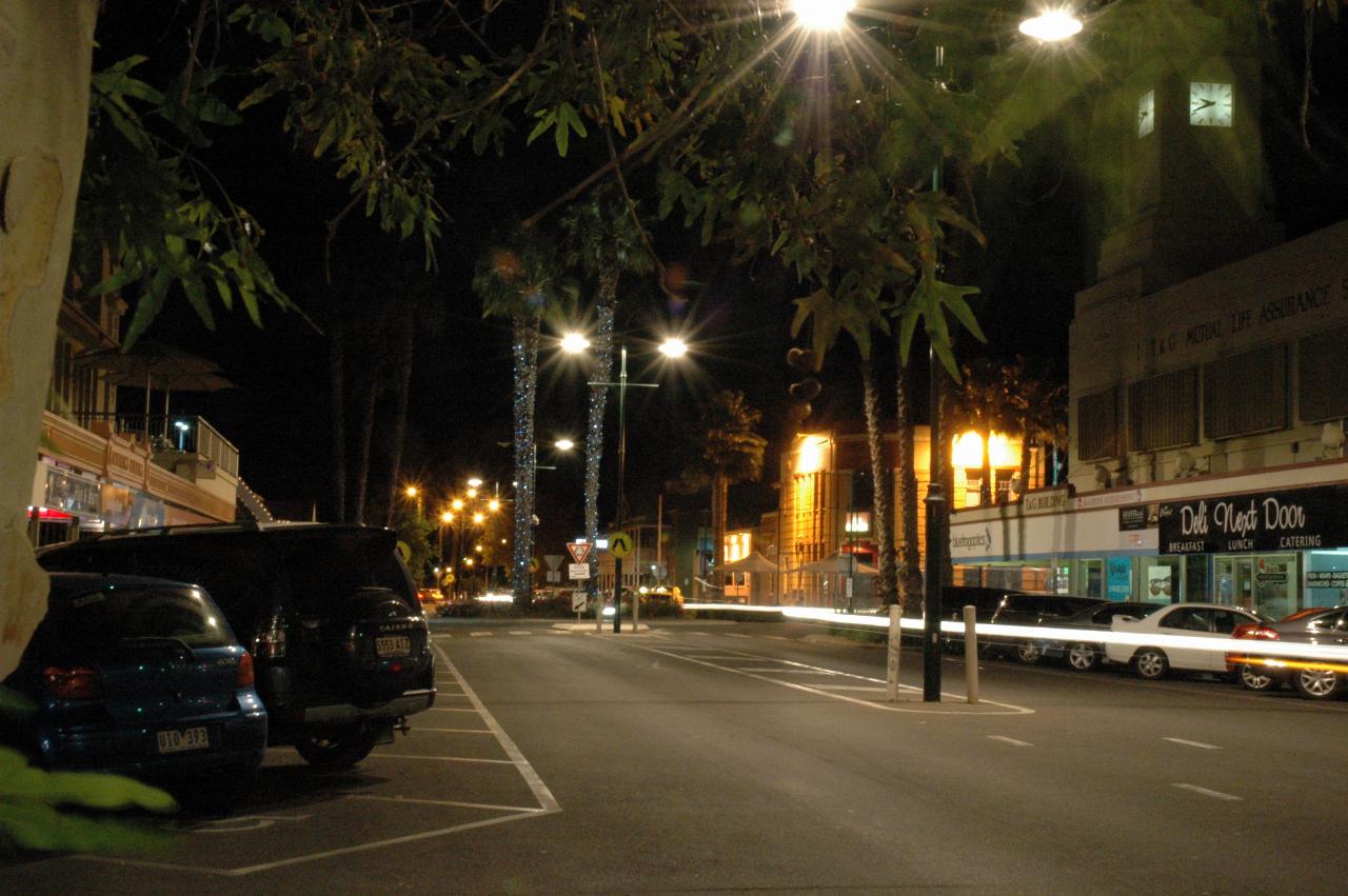 Long exposure photo of street, parked cars and illuminated palm trees in middle of street