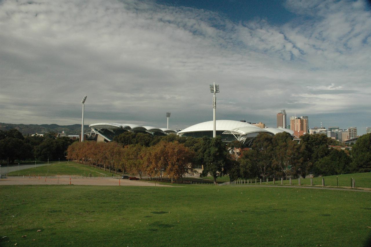 Grassy area leading to white scalloped roof building amidst trees, a few tall buildings behind