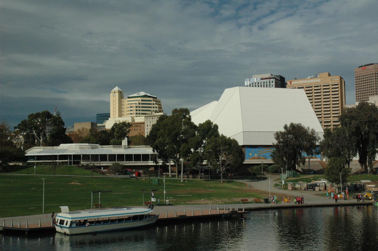 River in foreground, grassy hill and white buildings in front of other city buildings