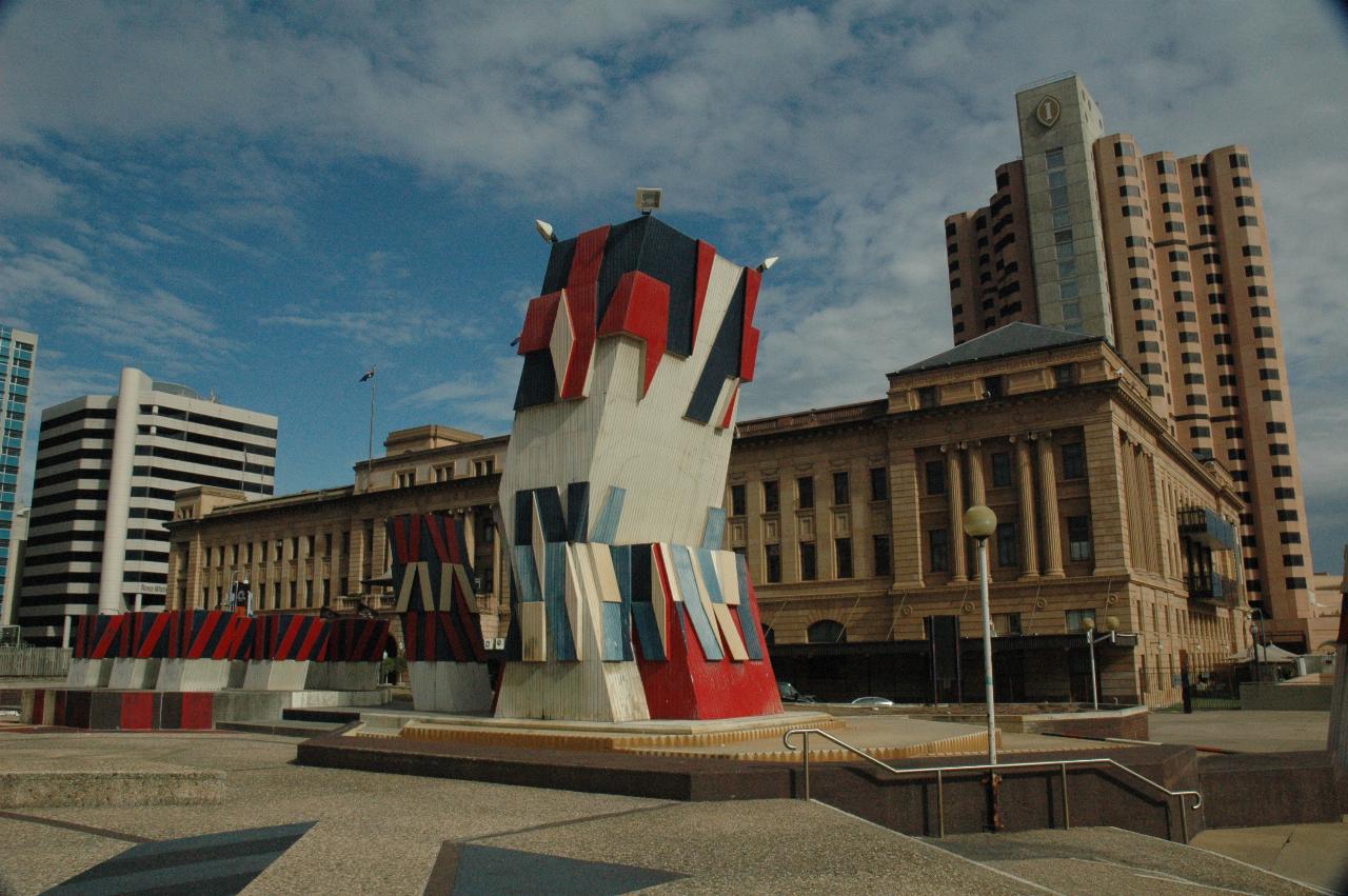 Plaza with bent tower type decoration, 4 storey stone building behind and high rise behind that
