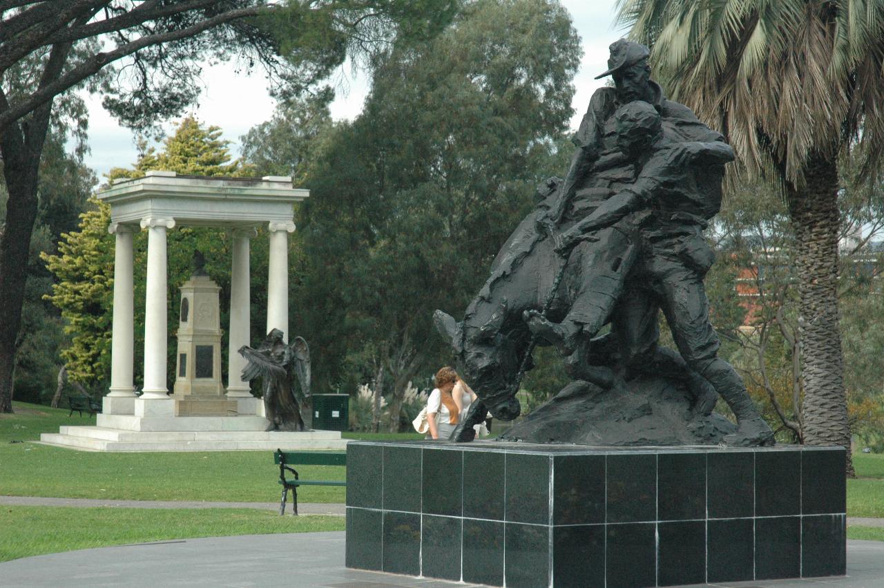 Statue of man on donkey and another helping, and in background another memorial stone column in shelter with greek columns
