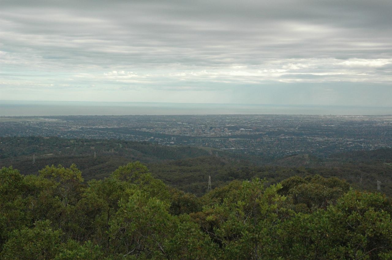 From hill top across tree covered hills with city on a plain and water beyond