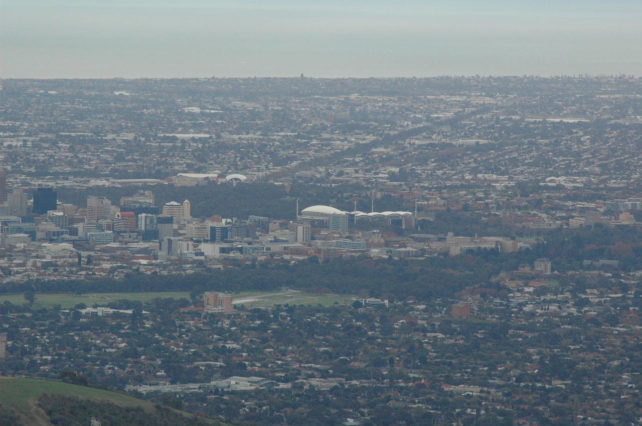 Foreground hills leading to city centre with tall buildings, then suburbia and water in distance