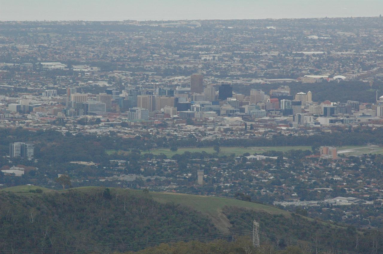 Foreground hills leading to city centre with tall buildings, then suburbia and water in distance