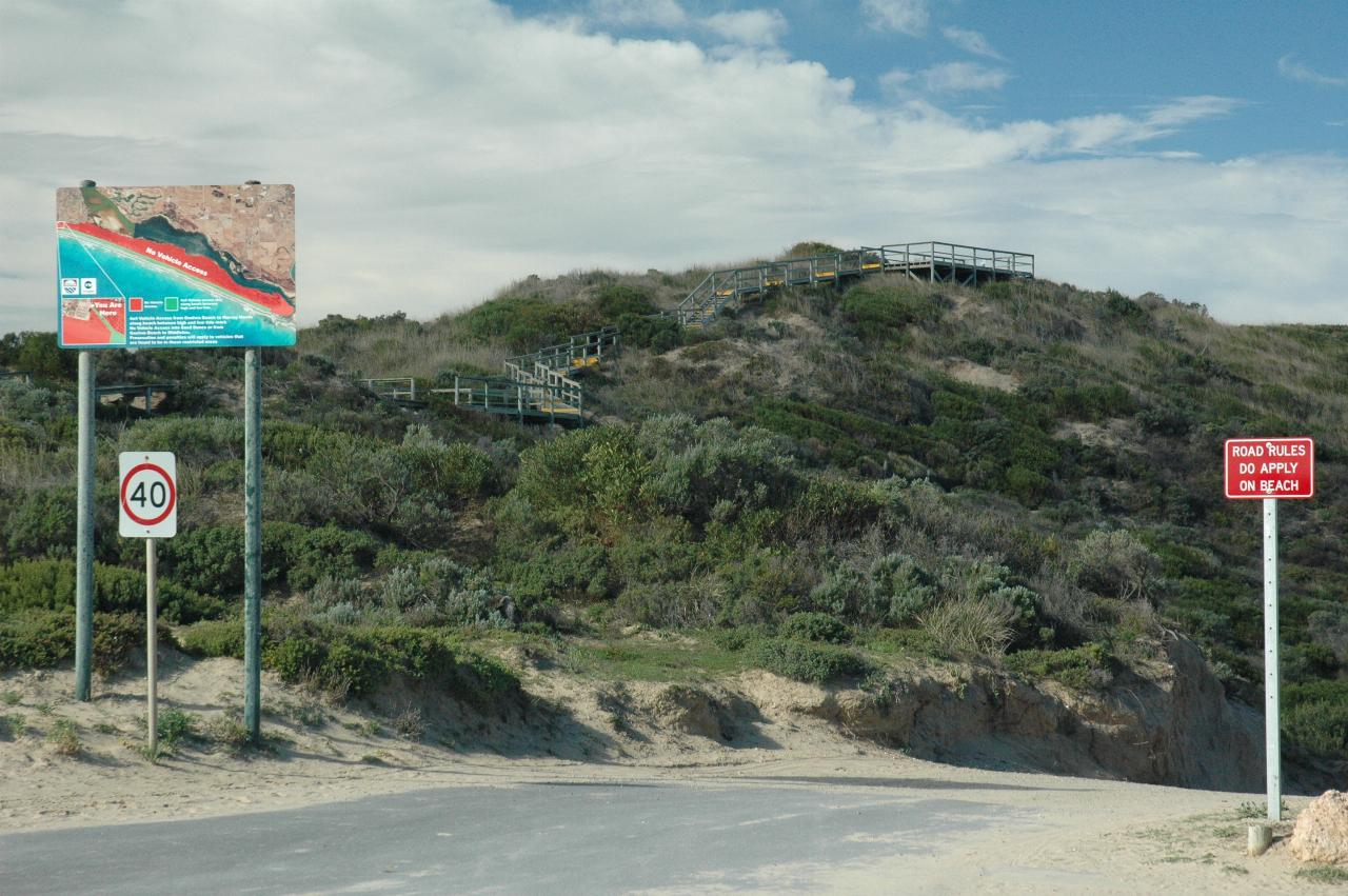 Sand hill covered in small shrubs, with wooden steps to wooden viewing platform at the top