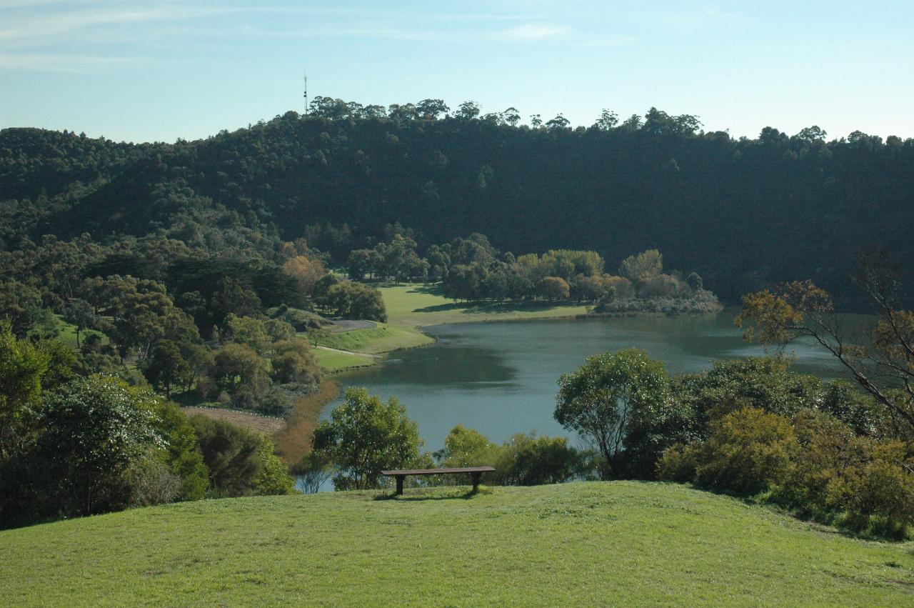 Grassy area with bench seat, looking down to small lake with distant crater rim