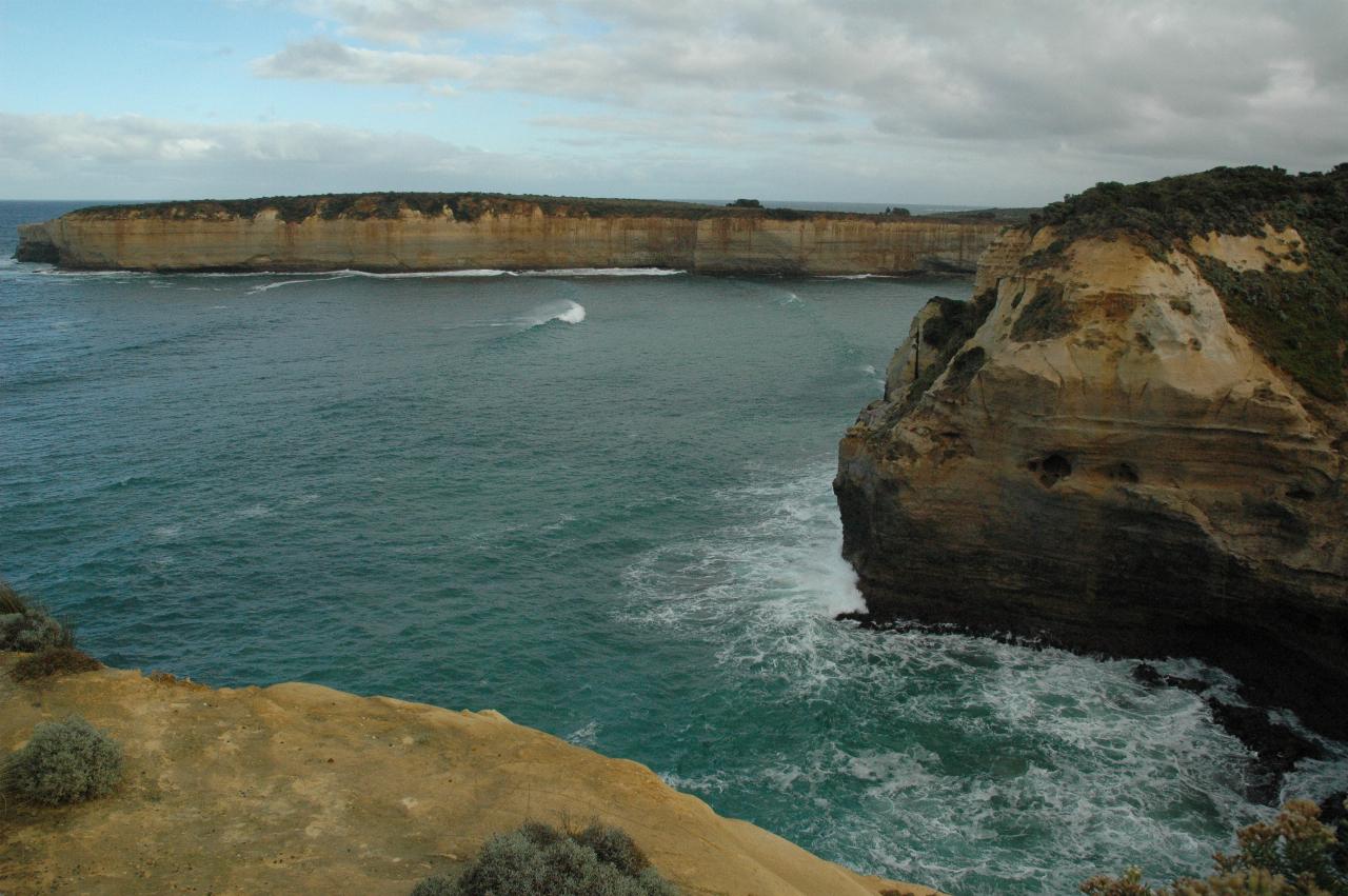 Small bay with ocean waves and ochre coloured cliffs with erosion