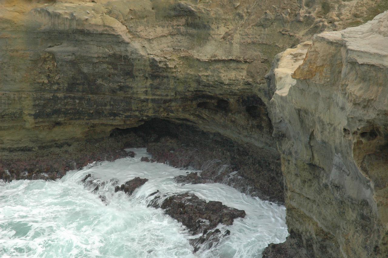 White water returning to ocean at base of cliff in small inlet which shows erosion at base
