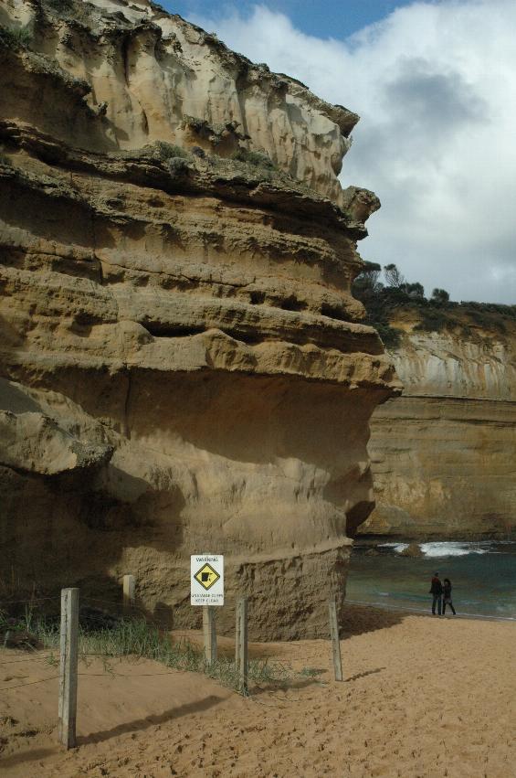 Two small figures near the base of a cliff with a sign nearby