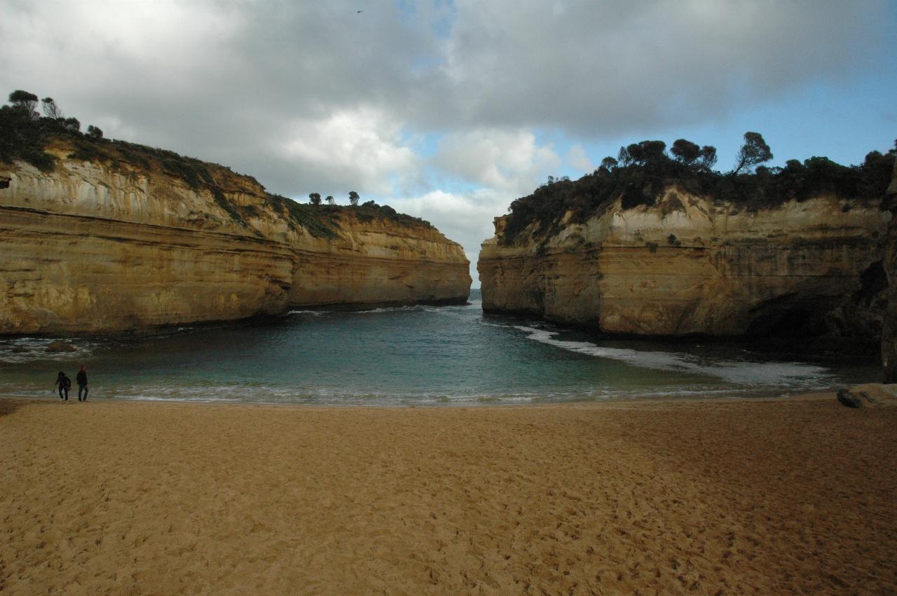 Two small figures on beach at head of long gorge opening to the sea