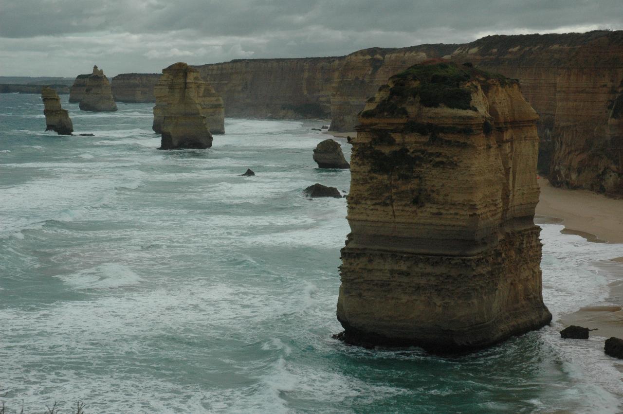 Tall coastal, ochre coloured cliffs with beach and waves, and varied shaped stacks in the ocean