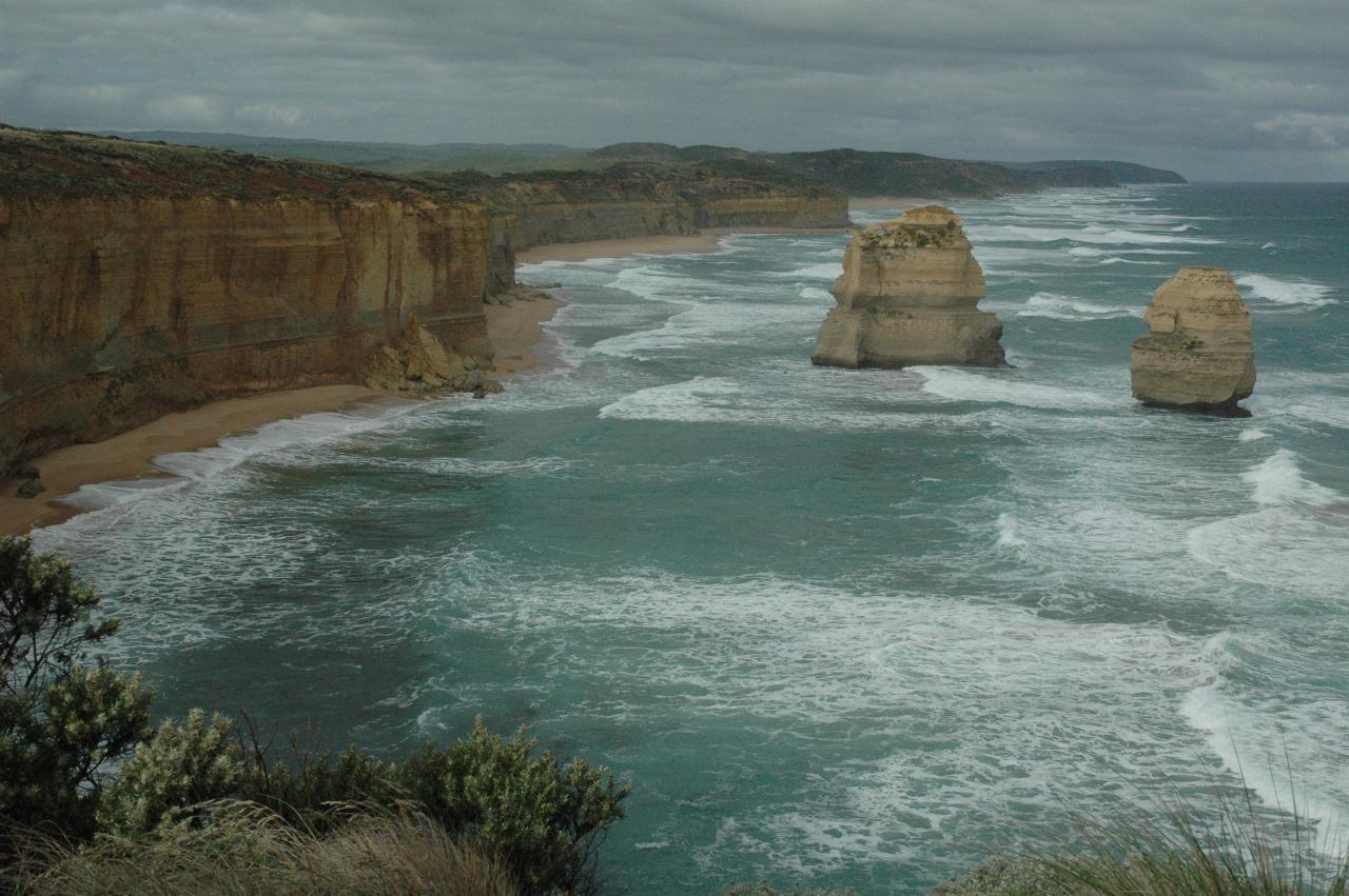 Tall coastal, ochre coloured cliffs with beach and waves, and varied shaped stacks in the ocean