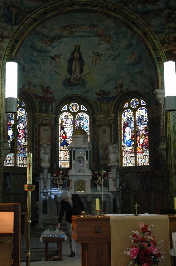 Portrait view of old altar and area behind it, including decorated walls and stained glass windows