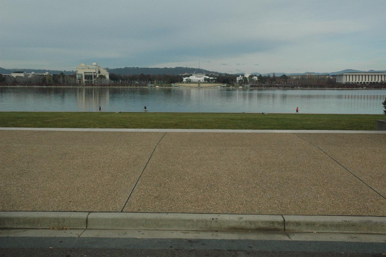 Grassy area leading to lake and buildings on far side, hill behind them