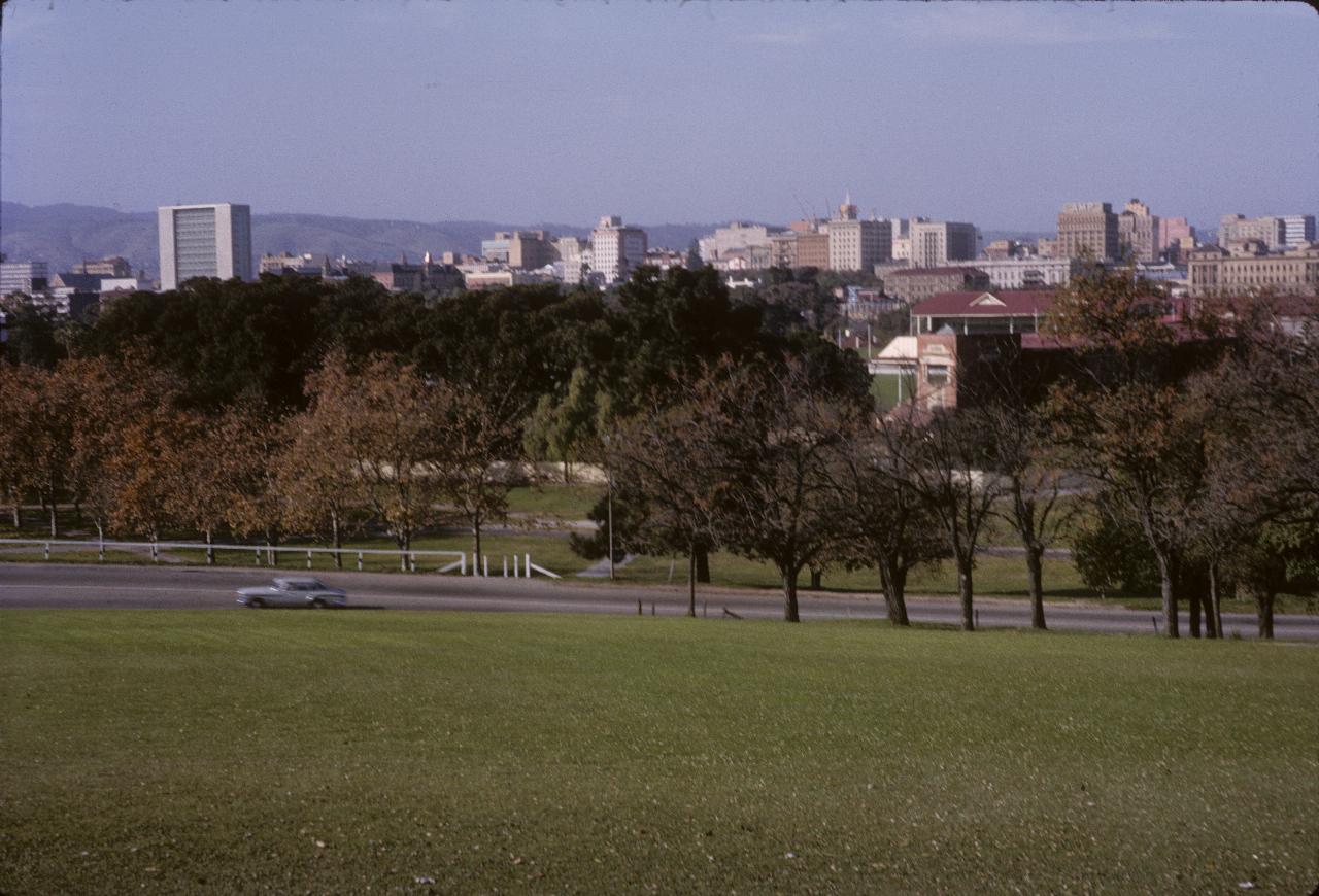 From grassy hill over sports ground to city low rise skyline to distant hills