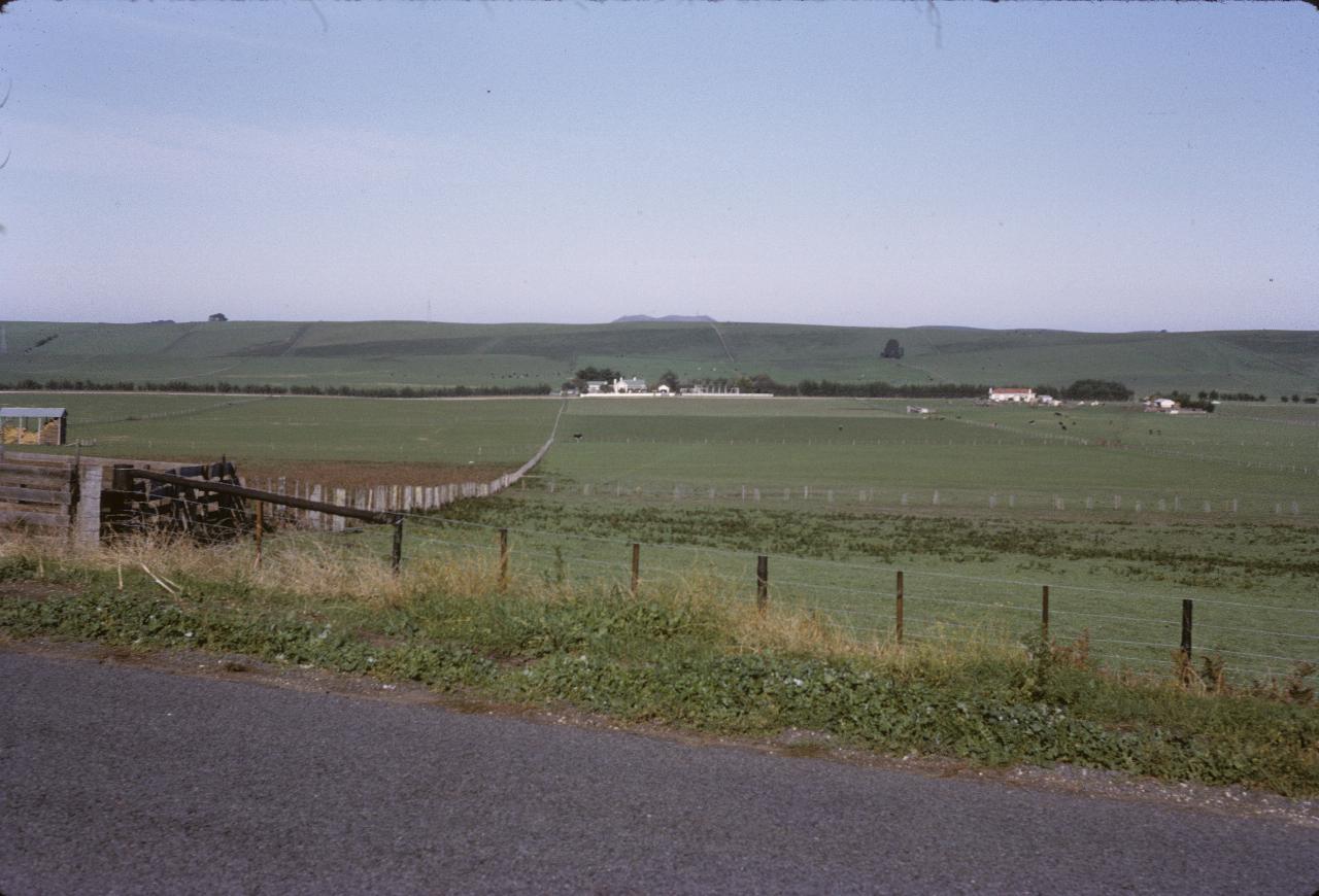 Green countryside to white farm buildings and green rising beyond