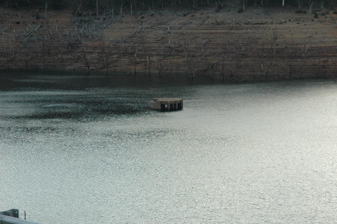 Cement circular object with flat top, pillars on sides, stick out of water in dam