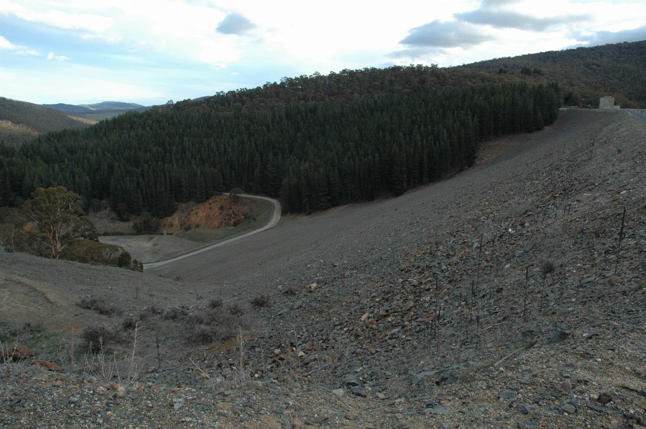 View down rocky face of front of dam wall to road and river below